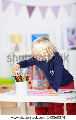 Little girl choosing colored pencil from organizer on table at home