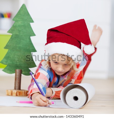 Little girl drawing Christmas decorations on chart paper while lying in house