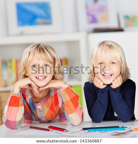 Portrait of happy siblings with drawing papers and pencils leaning on table at home