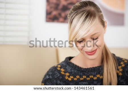 Smiling and shy beautiful blond woman looking down in a coffee shop wearing a knitwear sweater