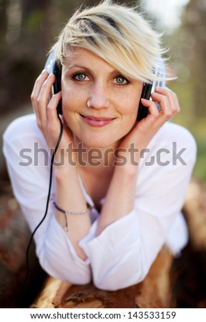 Closeup portrait of a beautiful young woman with headphones lying on log