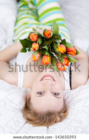 Smiling woman lying on bed and holding a bouquet of flower