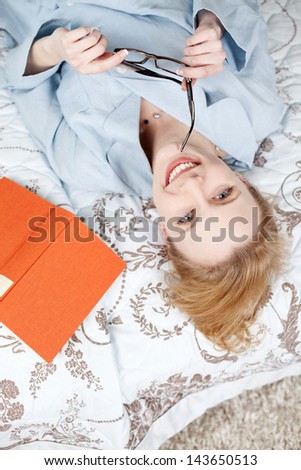 Image of a young woman relaxing in her bedroom and posing while reading a book.