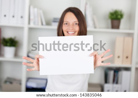 Happy woman shows the white empty paper inside the office