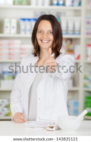 Portrait of confident female pharmacist gesturing thumbs up at pharmacy counter