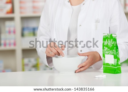 Midsection of female pharmacist crushing medicine in mortar at pharmacy counter