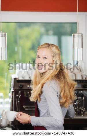 Portrait of happy waitress holding coffee cup against machine in cafe