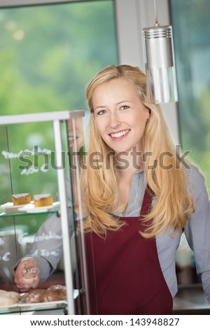 Portrait of happy waitress standing by display cabinet at coffee shop