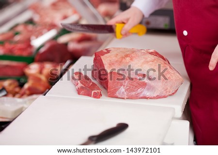 saleswoman with red apron cutting meat on board at counter