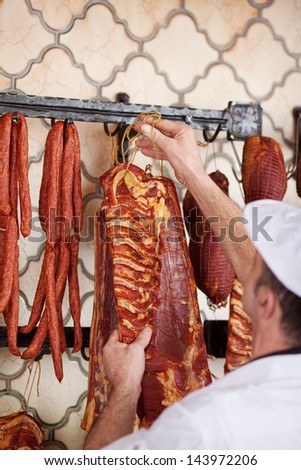 Male butcher hanging meat on hook in shop