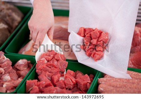 Closeup of butcher\'s hands packing meat pieces in paper at shop