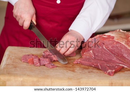 Midsection of butcher\'s hands cutting meat with knife in shop