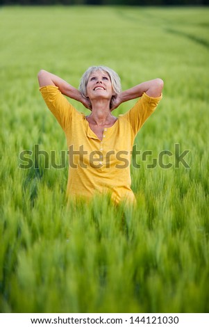 senior lady standing in corn field folding arms behind head