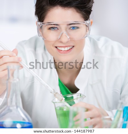 Portrait of confident female scientist wearing protective eyewear while experimenting at laboratory