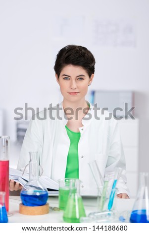 Portrait of confident female scientist with chemicals on desk in laboratory