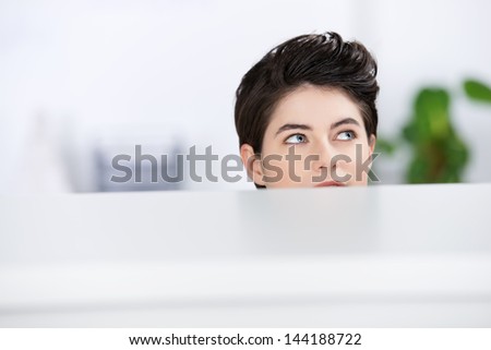 Closeup of young businesswoman looking away in cubicle at office