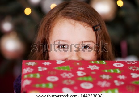 Laughing eyes pf a playful little girl with a Christmas gift peering over the top at the camera