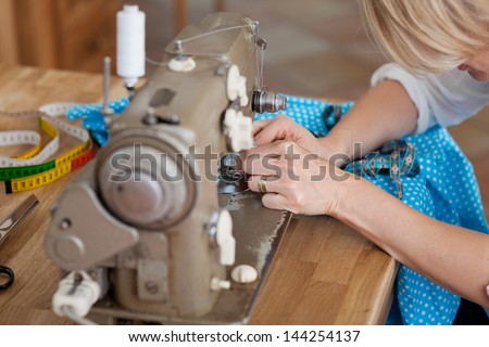 A woman sews blue fabric with machine