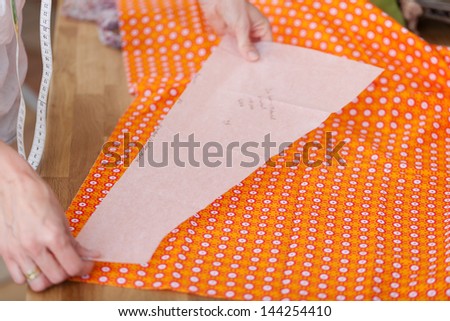 Tailor holds paper pattern on orange fabric
