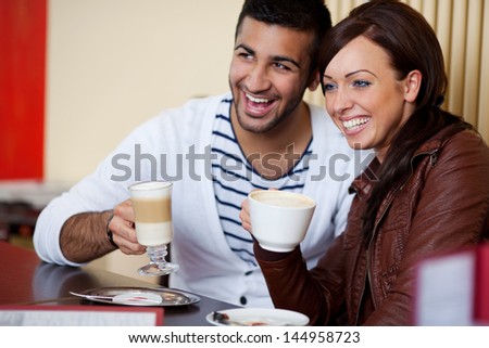 Laughing attractive young Asian couple in a sitting side by side at a table in a restaurant enjoying coffee together