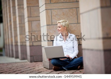 Full length of young woman with laptop sitting against column