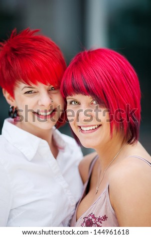 Two trendy fashion conscious young women with bright dyed red hair standing together smiling at the camera
