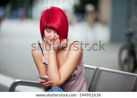 woman with red hair sitting ouside and writing sms