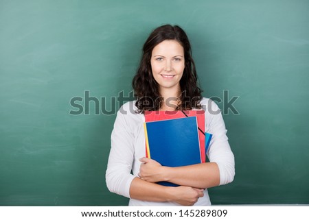 Portrait of young female teacher holding files against chalkboard in class