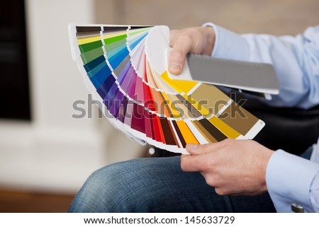 Man holding a set of paint color swatches in all the colors of the spectrum splayed out in his hand as he tries to decide on a new color for his house