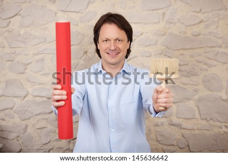 Confident male interior designer with a roll of orange wallpaper and a brush for applying the glue paste to the wall in his hands