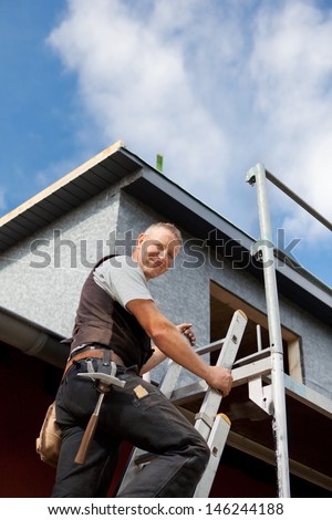 Smiling roofer climbing a ladder at the construction site