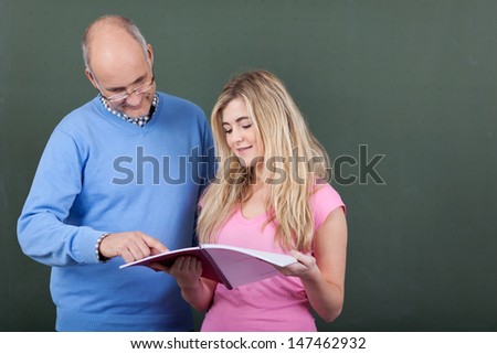 Male professor assisting female student in studies against chalkboard in classroom