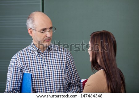 Middle-aged male lecturer and a young female student in a discussion standing close together in front of a blackboard chatting