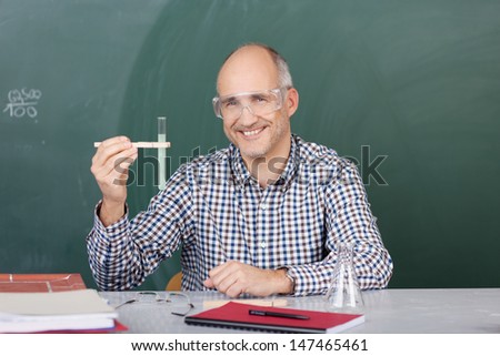 Laughing middle-aged male science teacher holding up a test tube with forceps to show his class the chemical reaction taking place