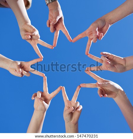 Low angle view of childrens hands forming a star with their fingers touching to the form the points against a clear blue sky, conceptual of teamwork and hope