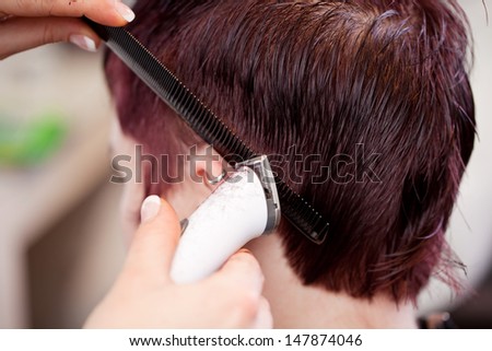 Hairstylist using a razor to trim the hair around a customers ear in a short neat hairstyle
