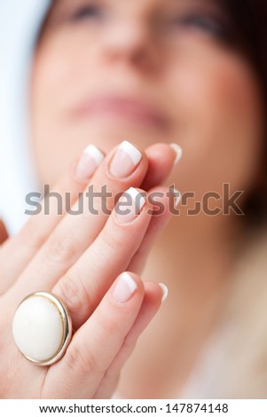 Close up view of a woman with manicured finger nails holding her palms together with her blurred face in the background