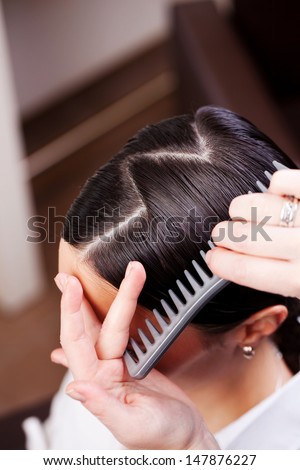 Closeup view of the hand and comb of a hairstylist combing a new hairstyle on a customer with a zig zag parting