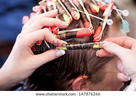 Closeup of the hands of a female hairstylist doing a perm rolling the clients hair onto fine rollers or curlers for a curly or wavy effect