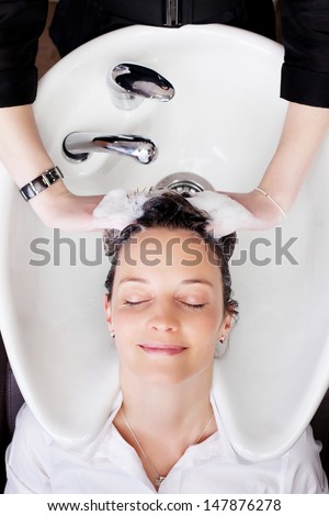 Overhead view of a woman having her hair shampooed at the hair salon smiling in bliss at the relaxing massage of the hairdressers fingers