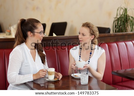 Two stylish beautiful young female friends sitting chatting in a cafe while enjoying cups of coffee