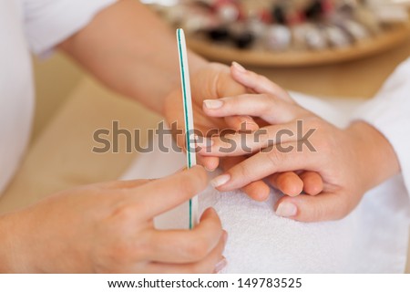 Beautician doing a manicure filing the finger nails of a client in the salon, cropped view of their hands