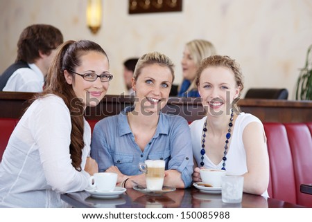 Happy three young female friends enjoying a cup of cofee at a cafeteria