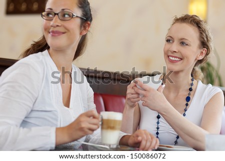 Two attractive young female friends enjoying themselves over coffee in a cafe looking to the side as they laugh and smile