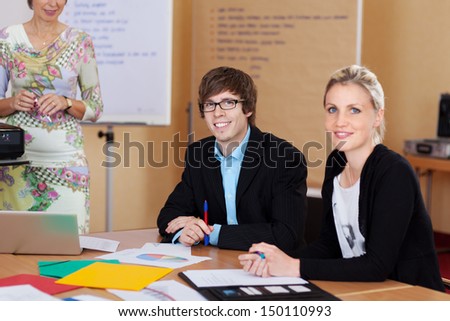 Two young trainees, a man and woman, sitting at a table working during class in business school