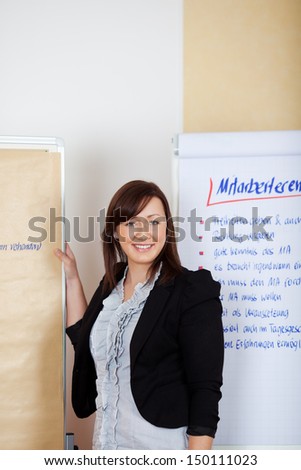 Confident cheerful professional female employee standing in front of the paperboards in the office
