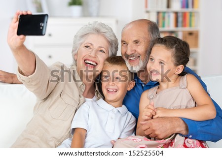 Grandparents and grandchildren sitting together in a close group on a sofa laughing and doing a self portrait with a hand held camera on a mobile phone