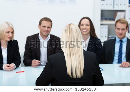 Young female job applicant in an interview sitting with her back to the camera facing a row of personnel executives