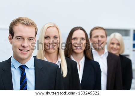 Serious handsome young business manager with his successful team of diverse business people lined up behind him