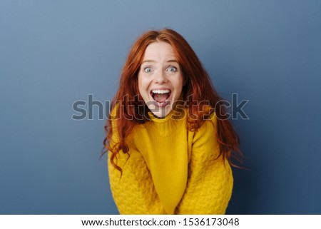 Laughing delighted young woman leaning forwards towards the camera with a look of amazement and awe over a blue studio background with copy space Foto stock © 